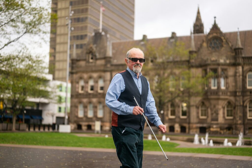 Elderly blind man walking with a white cane.
